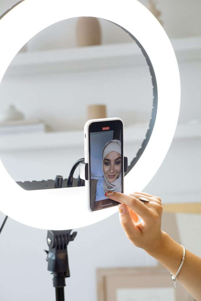 ژنێک کە ڤیدیۆیەک لەسەر مۆبایلێکی زیرەک تۆمار دەکات بە بەکارهێنانی ڕێکخستنی ڕووناکی ئەڵقە بۆ دروستکردنی ناوەڕۆک.