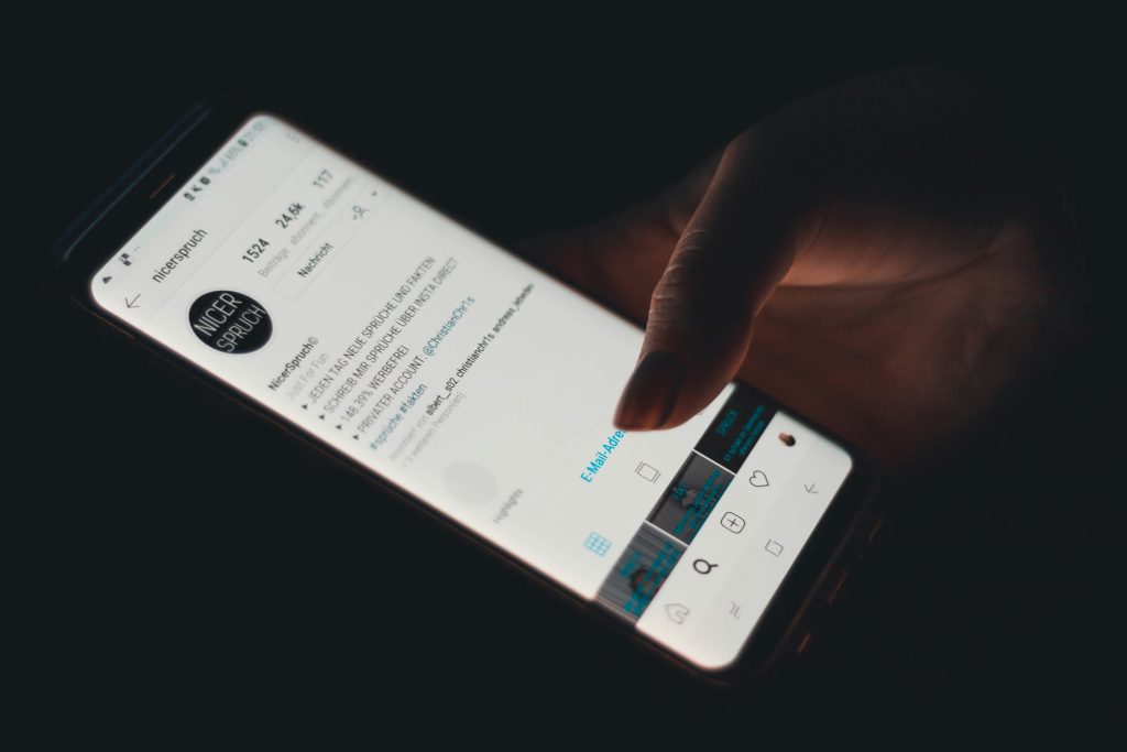 دەستێک لەسەر مۆبایلێک دەست دەگرێت کە پرۆفایلی ئینستاگرامی Nice Scrubs لەسەر شاشەکەی دیارە، لەگەڵ ئامێری دەستکاریکردنی وێنە لە خوارەوەی شاشەکە